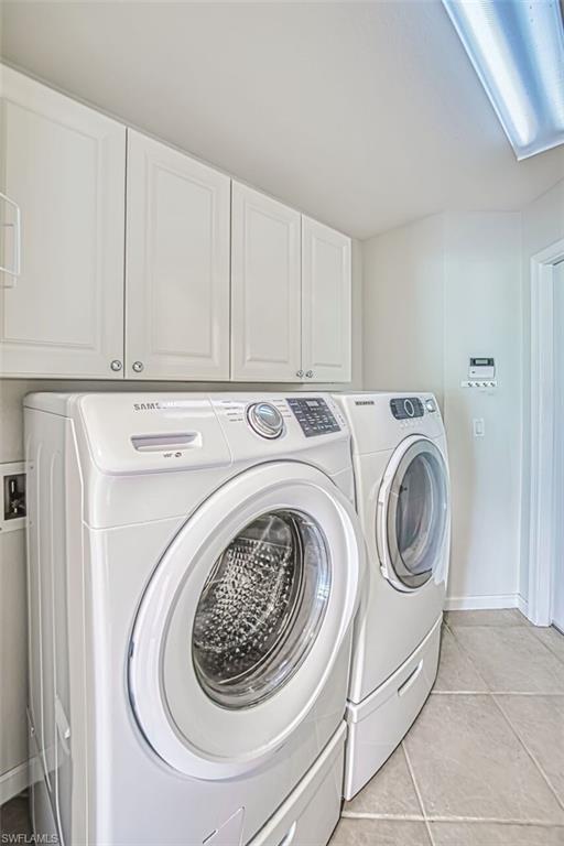 Laundry area featuring light tile patterned floors, cabinet space, and washing machine and clothes dryer