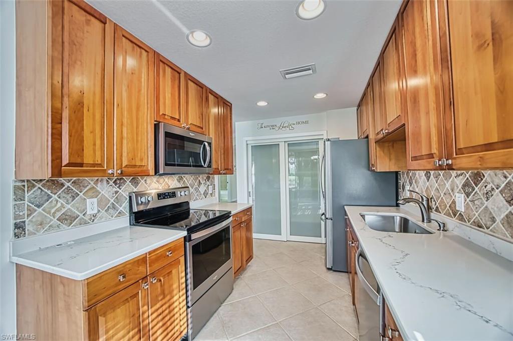 Kitchen with brown cabinetry, stainless steel appliances, light stone counters, light tile patterned floors, and recessed lighting