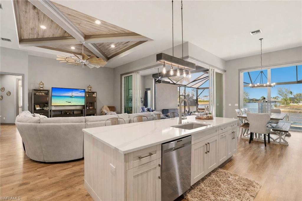 From the kitchen, you can watch the family inside and outside.  Kitchen featuring a chandelier, stainless steel dishwasher, light stone countertops, open floor plan, and light wood-style flooring.