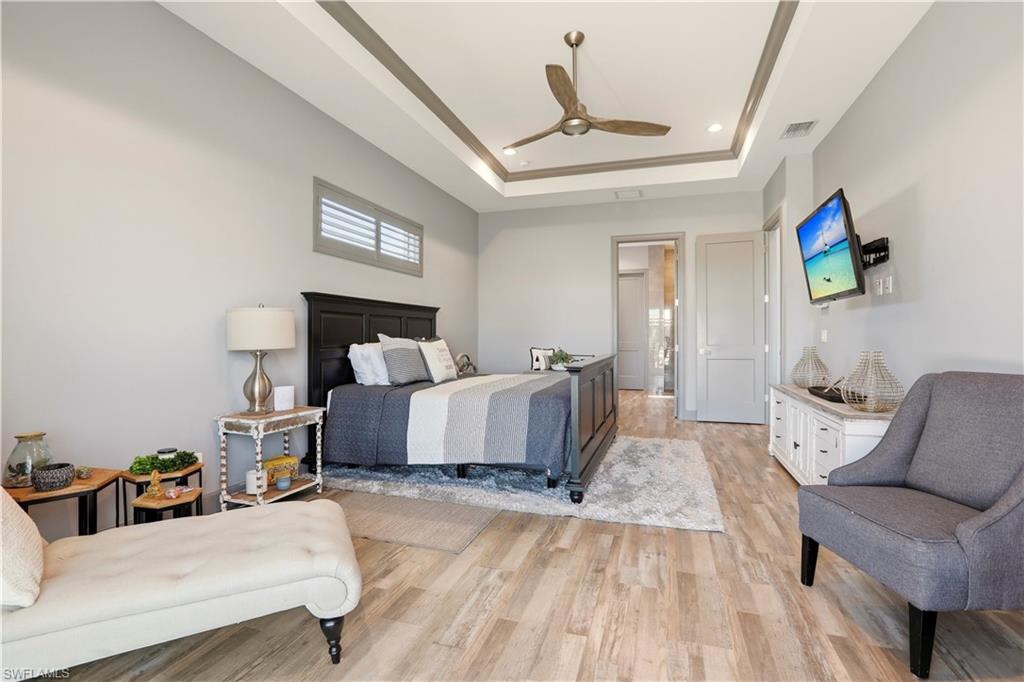 Primary Bedroom with light wood finished floors, a ceiling fan, recessed lighting, and a raised ceiling