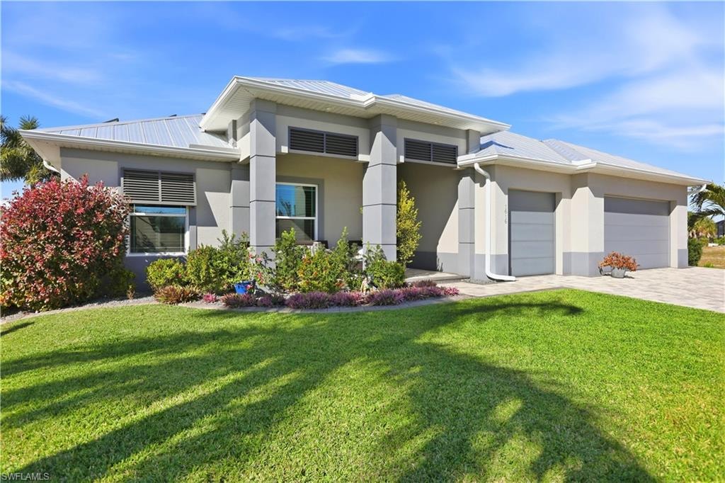 Front elevation with a nicely landscaped front yard, a 3 car garage, steel roof, stucco siding, and decorative driveway.