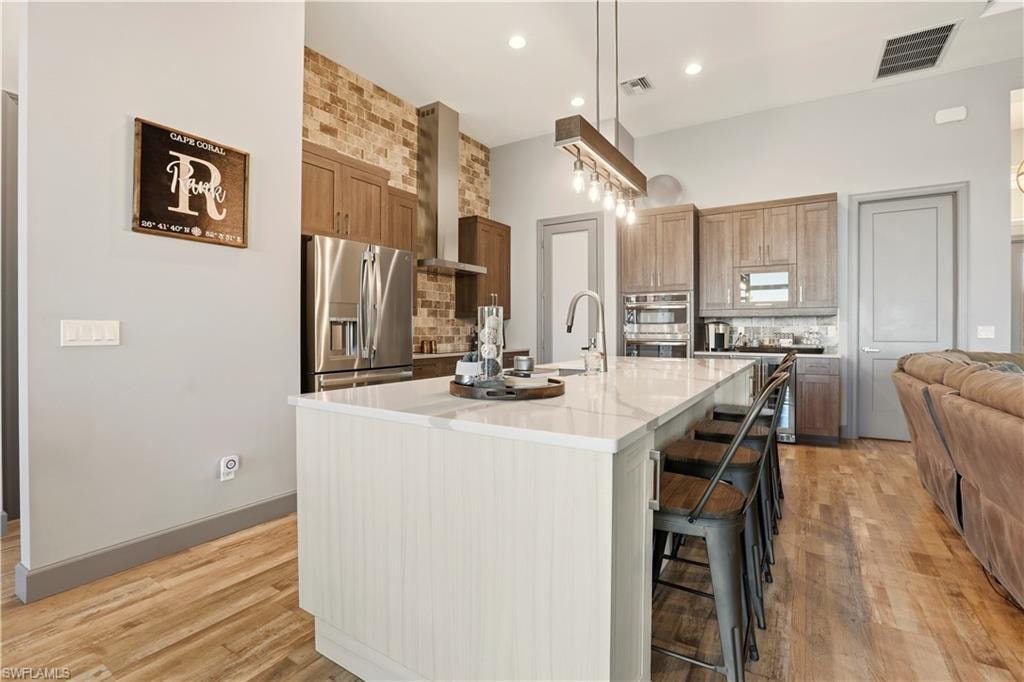Kitchen featuring tasteful New York SOHO Brick backsplash, a kitchen breakfast bar, high end appliances with stainless steel finishes, an island with Pompei Luxury Quartz Counters with Stainless Steel sink, and light wood finished floors.
