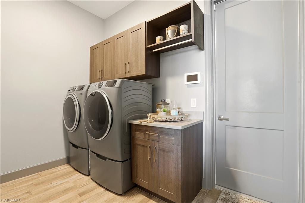 Laundry area featuring light wood-style flooring, washer and dryer, and cabinet space