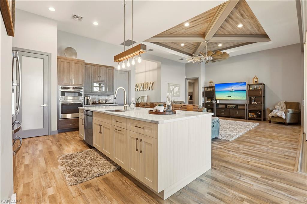 Large pantry on the left side of this pic, double oven, wine refrigerator on the far wall.  Kitchen featuring open floor plan, light brown and dove white solid cabinets, hanging light fixtures, light wood-style floors, and recessed lighting