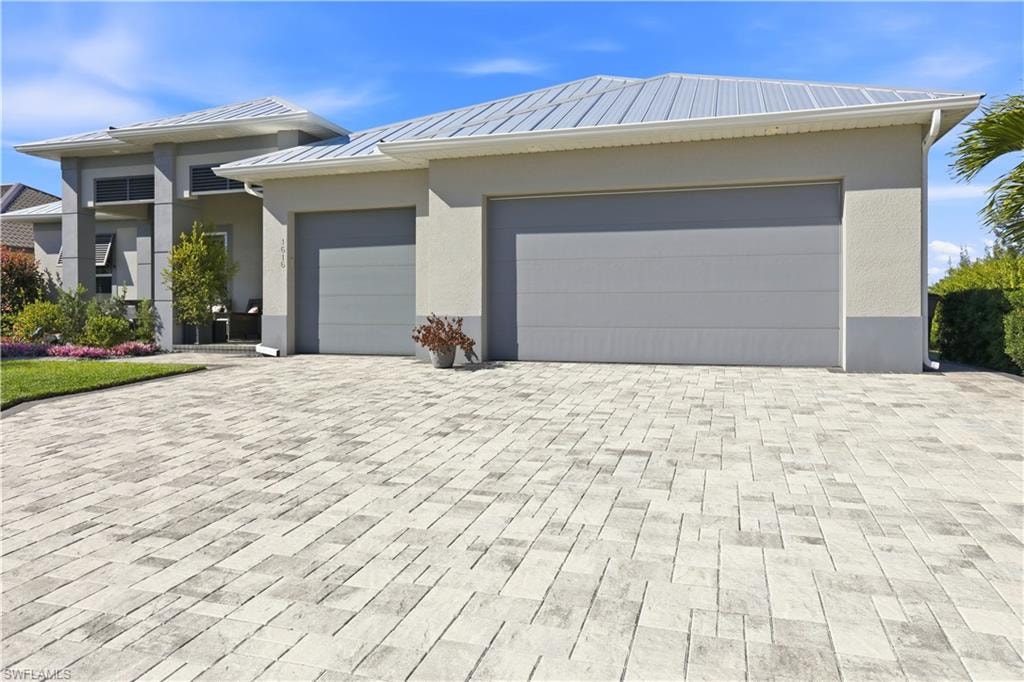 View of front of house featuring decorative stone driveway, a metal roof, a 3 car garage, and stucco siding
