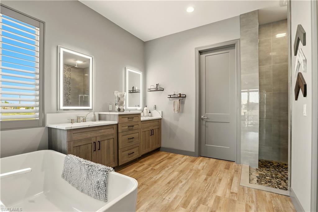 Primary Full bathroom featuring a walk in shower, double sink vanity, light wood-style flooring, a freestanding bath, and recessed lighting