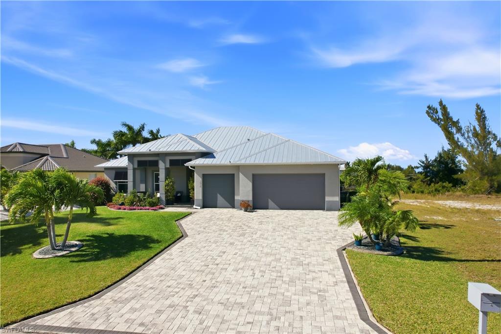 View of front of house with decorative driveway, a front yard, a 3 car garage and a metal roof.