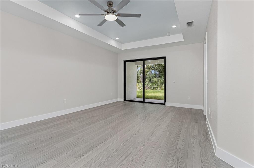 Spare room with a tray ceiling, light wood-type flooring, recessed lighting, and ceiling fan