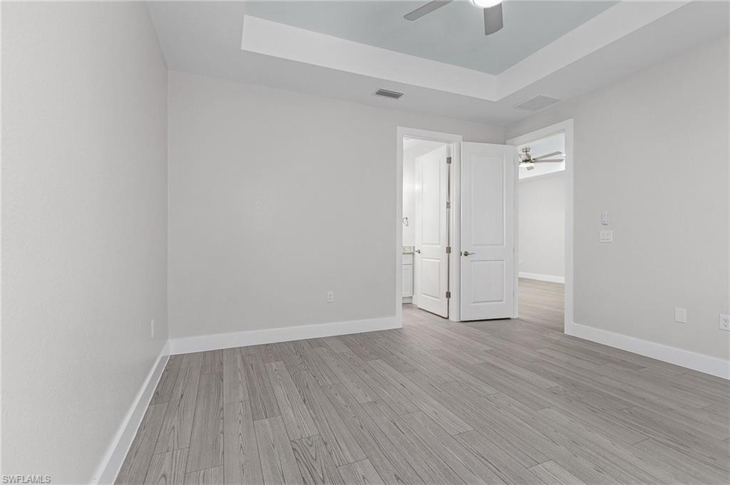 Unfurnished bedroom with a raised ceiling, light wood-style floors, ceiling fan, and ensuite bath