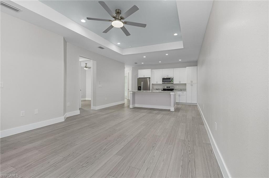Unfurnished living room with ceiling fan, recessed lighting, a tray ceiling, and light wood finished floors