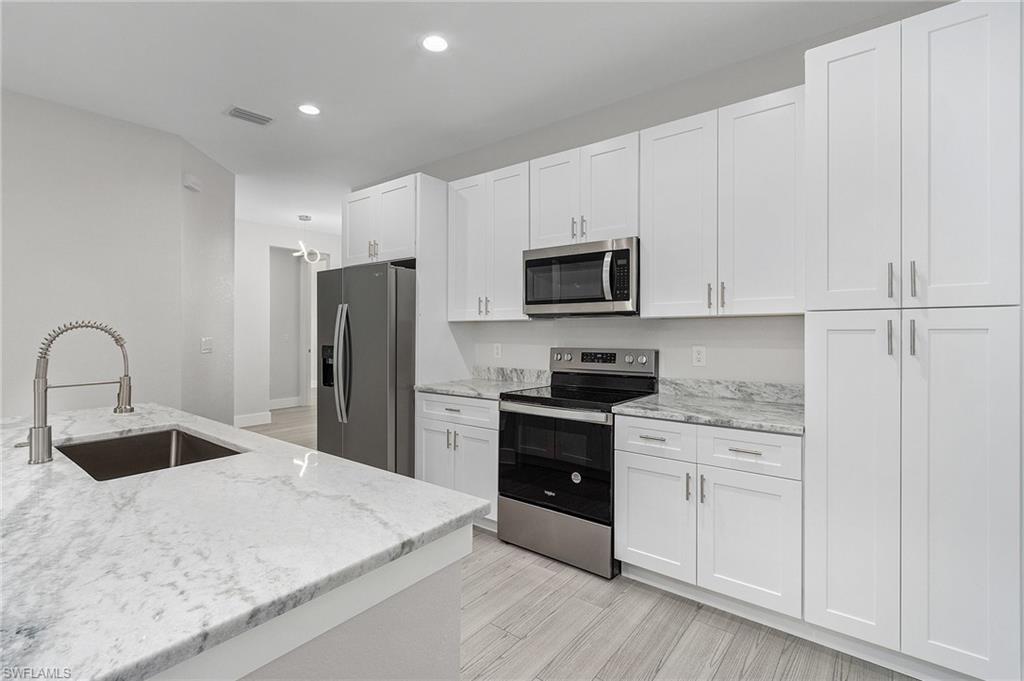 Kitchen featuring appliances with stainless steel finishes, light stone counters, white cabinets, light wood-style flooring, and recessed lighting