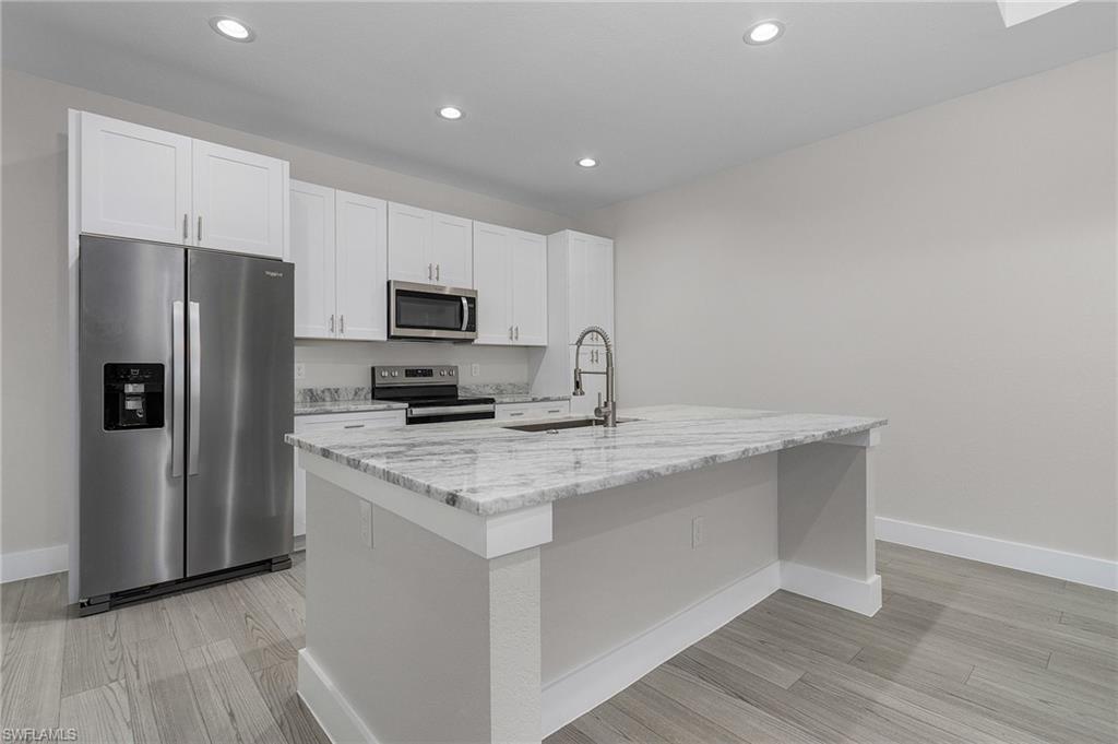 Kitchen with appliances with stainless steel finishes, light stone counters, white cabinets, a center island with sink, and light wood finished floors