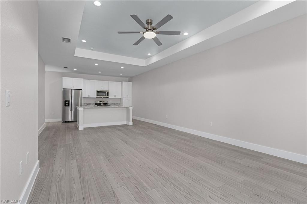 Unfurnished living room featuring recessed lighting, light wood finished floors, a ceiling fan, and a tray ceiling