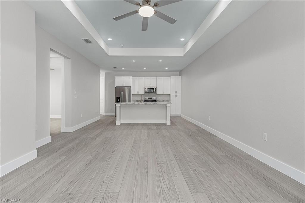 Unfurnished living room with a tray ceiling, recessed lighting, light wood-style floors, and a ceiling fan