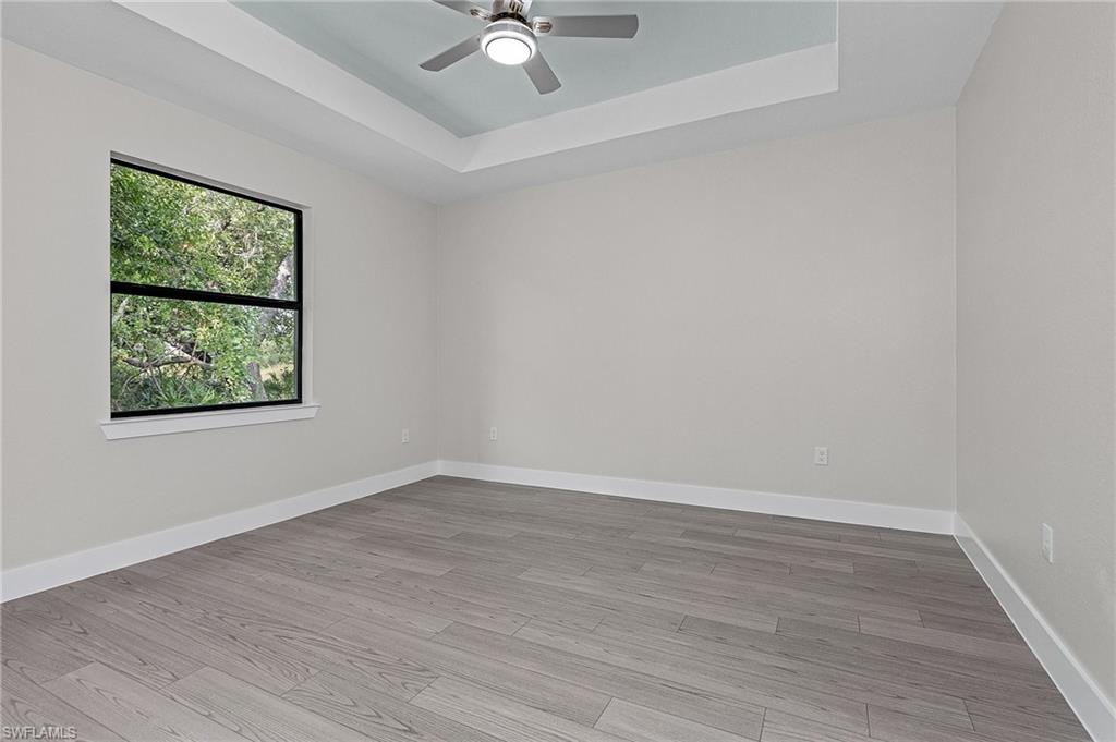 Spare room with a raised ceiling, light wood-style flooring, and ceiling fan