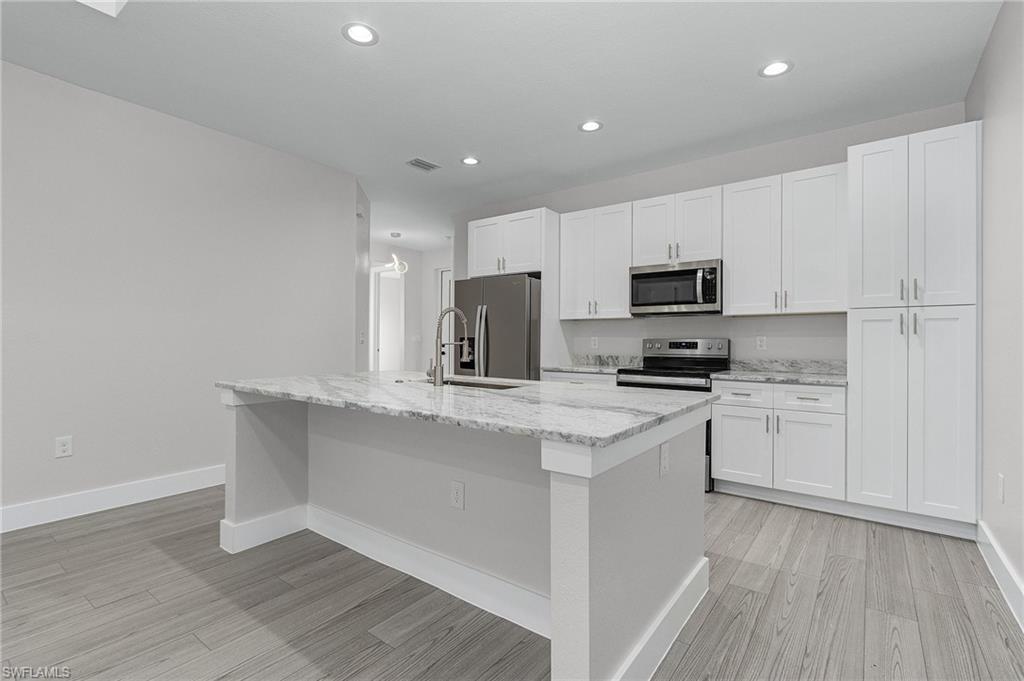 Kitchen featuring light stone countertops, an island with sink, appliances with stainless steel finishes, white cabinetry, and recessed lighting