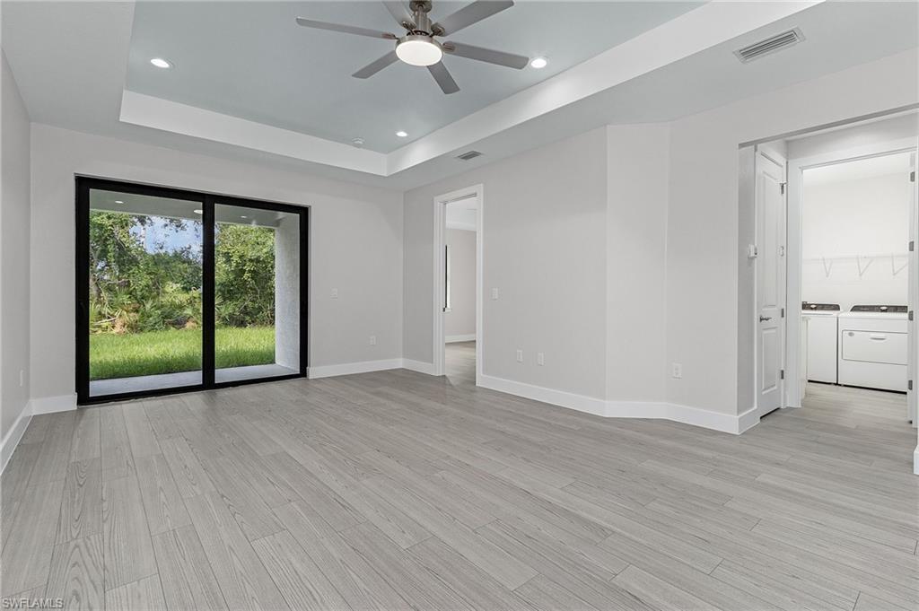 Empty room with washer and dryer, recessed lighting, a raised ceiling, light wood-type flooring, and ceiling fan