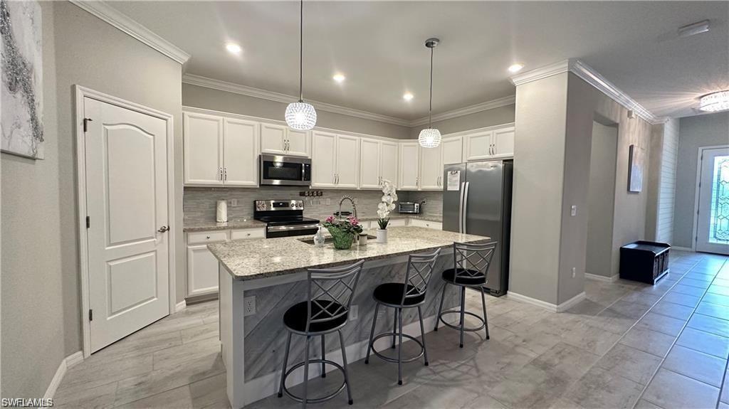 Kitchen featuring light stone counters, a kitchen island with sink, stainless steel appliances, white cabinetry, and hanging light fixtures