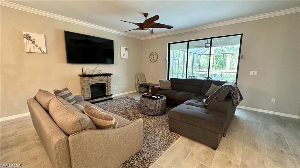 Living area featuring baseboards, a fireplace, a ceiling fan, and crown molding