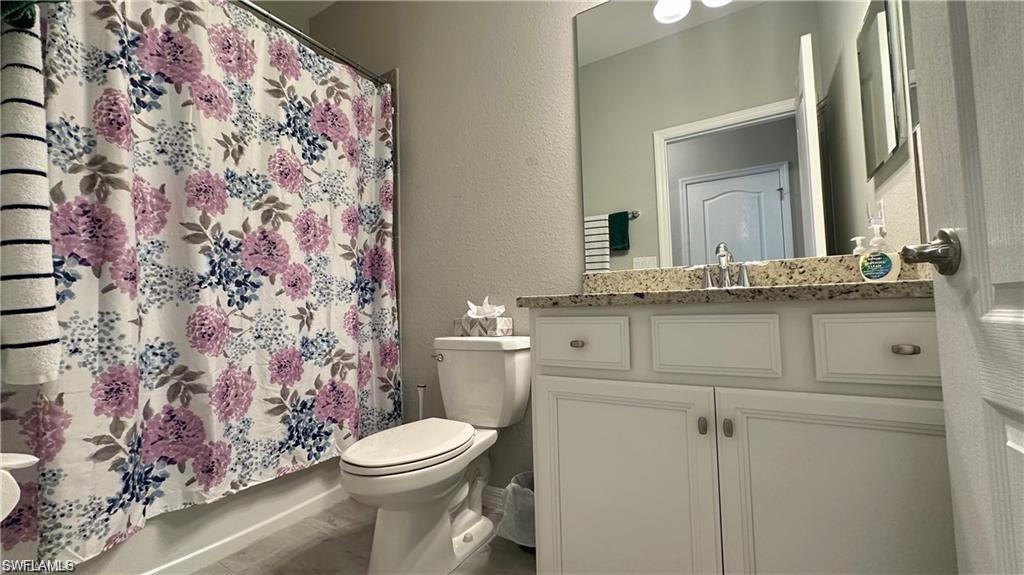 Bathroom featuring toilet, a textured wall, curtained shower, and vanity
