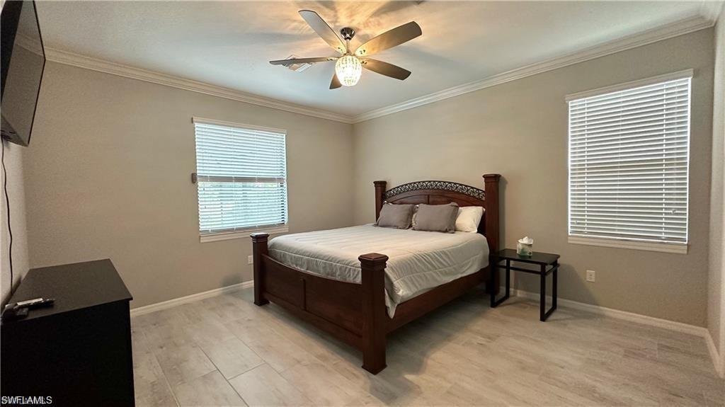 Bedroom with ornamental molding, light wood finished floors, baseboards, and a ceiling fan