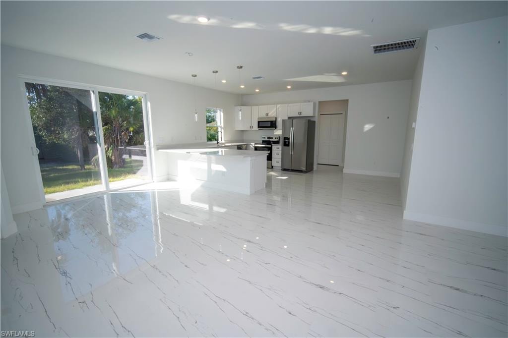 Kitchen with white cabinetry, stainless steel appliances, decorative light fixtures, open floor plan, and light marble finish floors