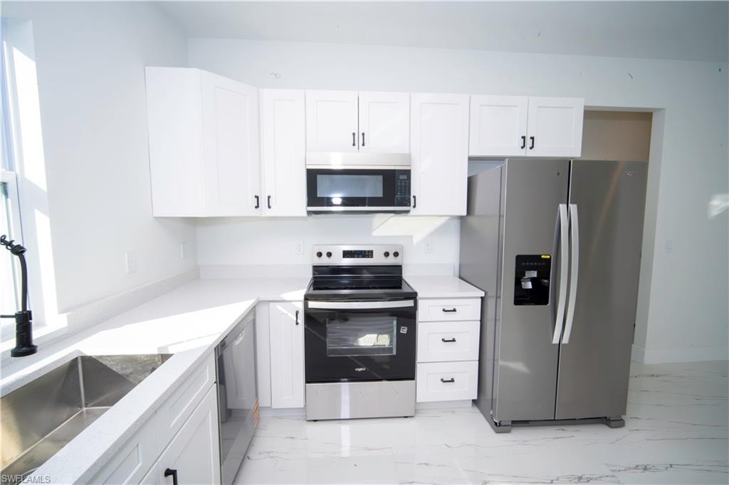 Kitchen with stainless steel appliances, white cabinets, light stone counters, and light marble finish floors