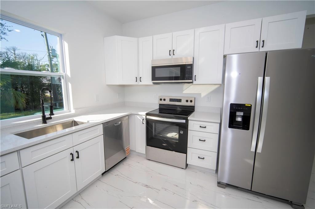Kitchen with appliances with stainless steel finishes, white cabinetry, light stone counters, and light marble finish flooring