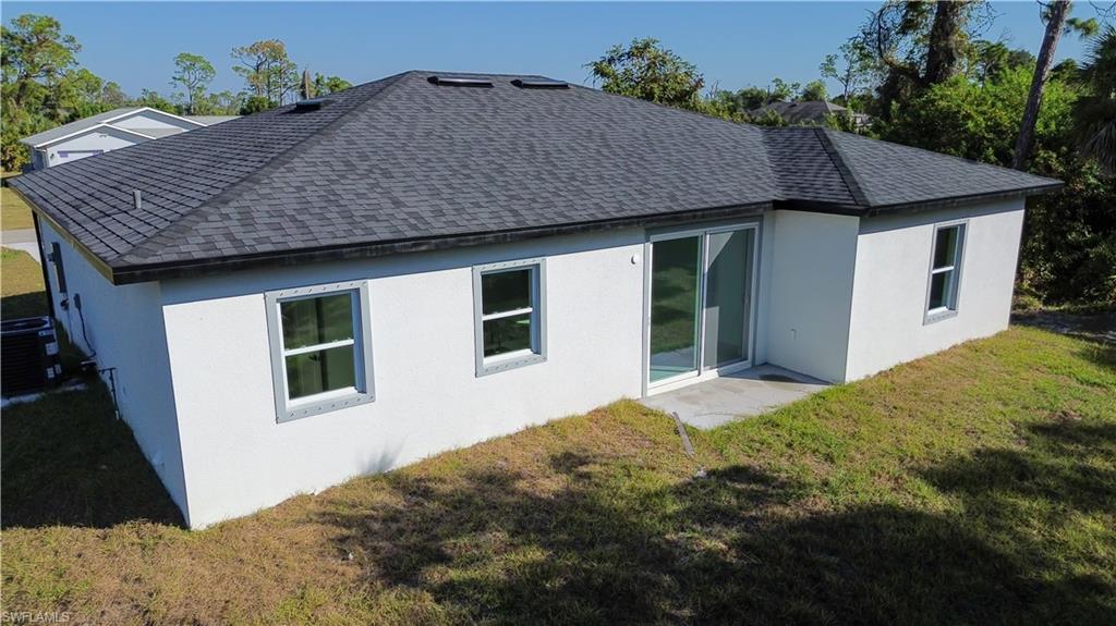 Rear view of property featuring a yard, stucco siding, a shingled roof, and a patio area