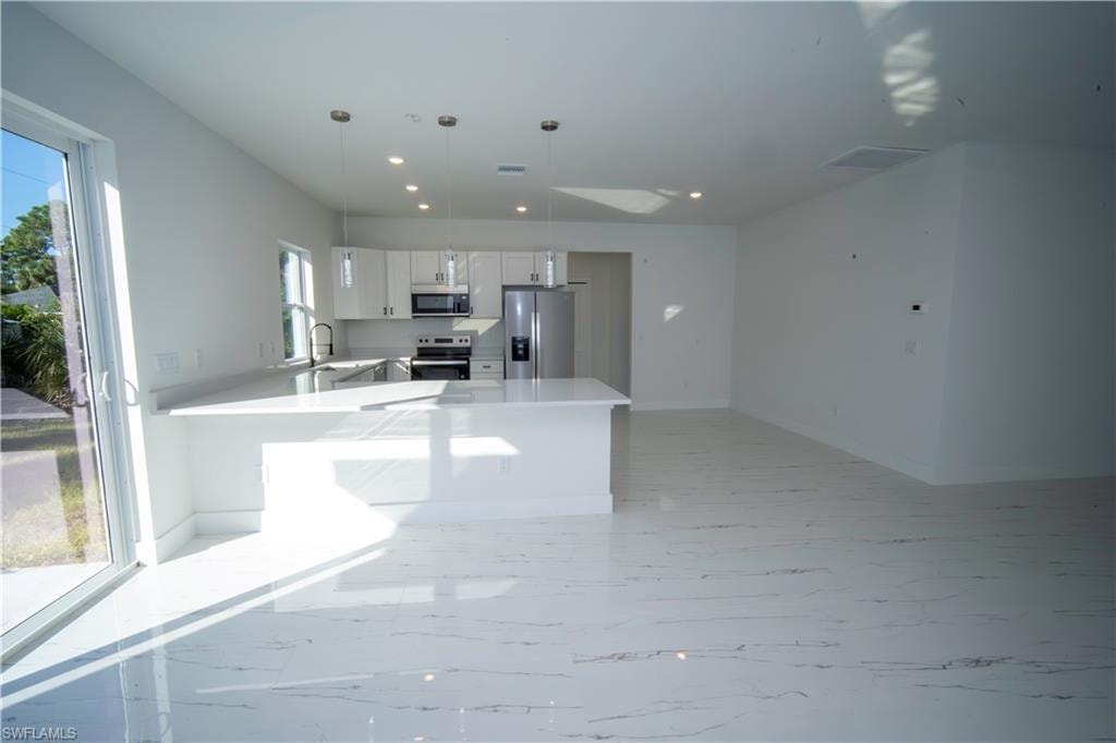 Kitchen featuring white cabinetry, a peninsula, appliances with stainless steel finishes, pendant lighting, and light stone countertops