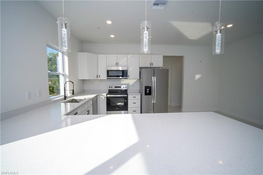 Kitchen with stainless steel appliances, white cabinetry, decorative light fixtures, light stone countertops, and recessed lighting