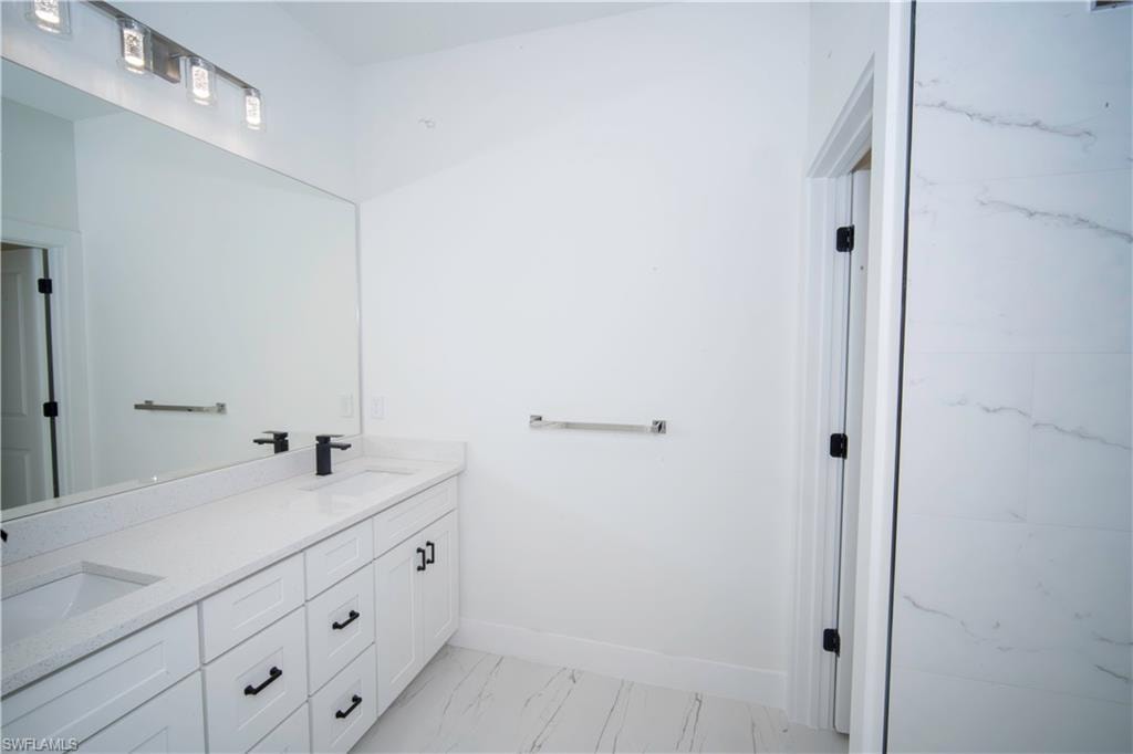 Full bath featuring double vanity and light marble finish floors