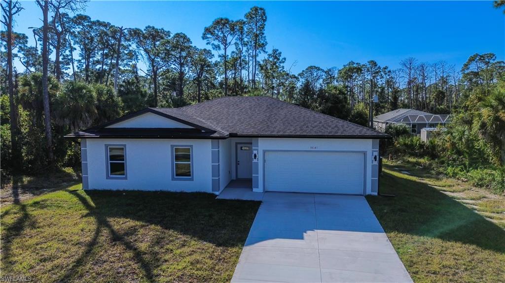 Single story home featuring a front lawn, driveway, stucco siding, an attached garage, and view of scattered trees