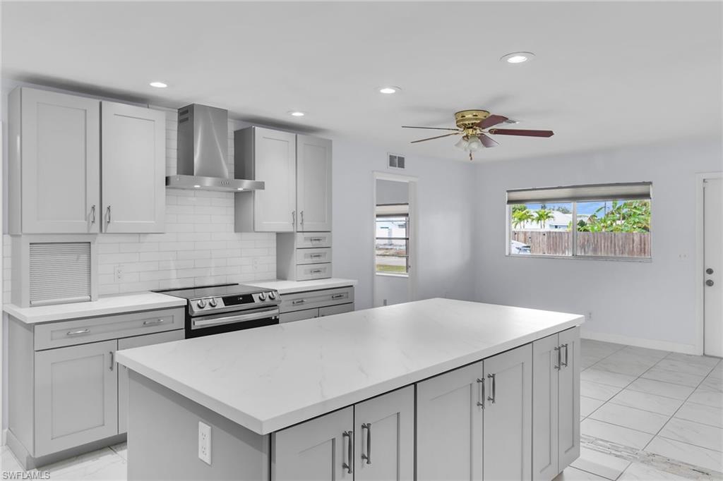 Kitchen with wall chimney range hood, electric stove, a kitchen island, backsplash, and recessed lighting