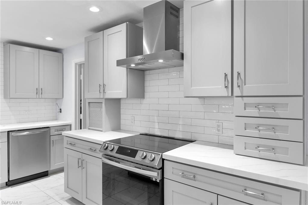 Kitchen with stainless steel appliances, wall chimney exhaust hood, light marble finish flooring, light stone counters, and decorative backsplash