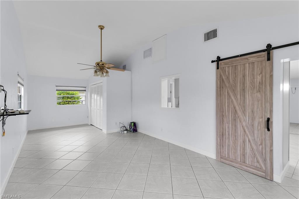 Unfurnished living room with high vaulted ceiling, a ceiling fan, a barn door, and light tile patterned floors