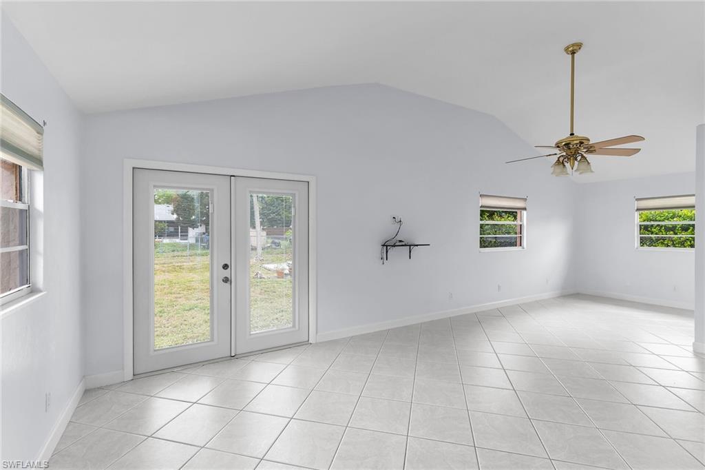 Empty room with a ceiling fan, light tile patterned floors, french doors, and lofted ceiling