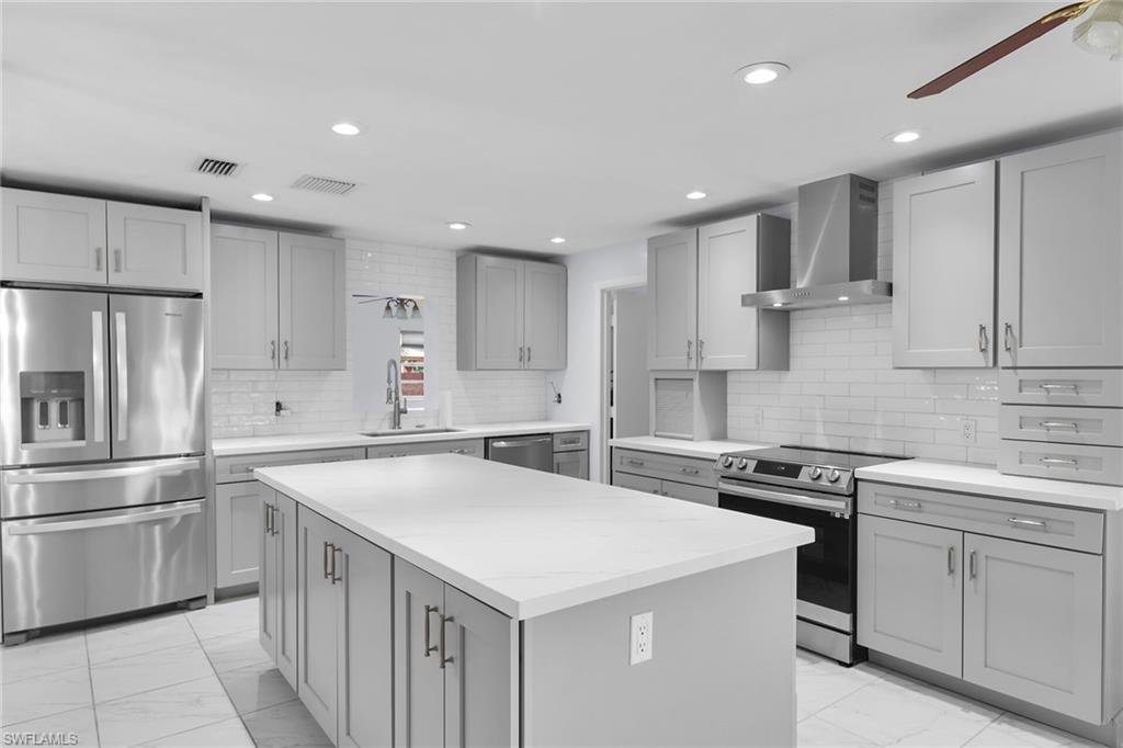 Kitchen with stainless steel appliances, a ceiling fan, gray cabinets, wall chimney exhaust hood, and light marble finish flooring