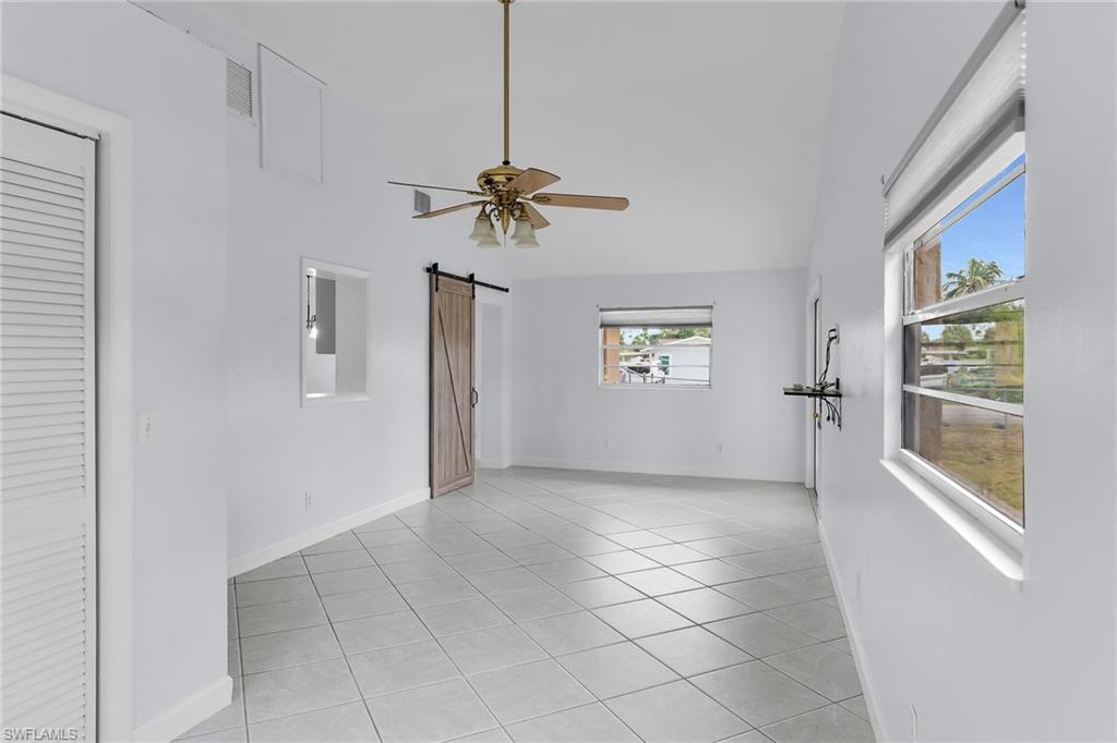 Unfurnished room featuring a barn door, light tile patterned flooring, ceiling fan, and high vaulted ceiling
