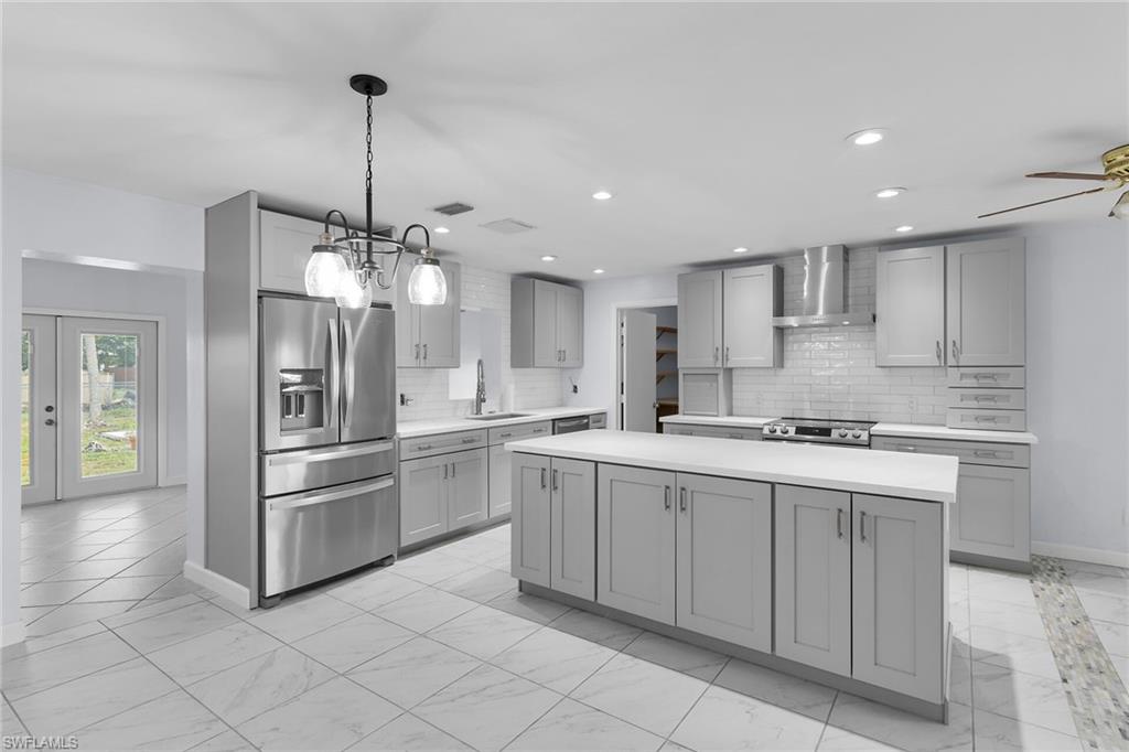 Kitchen featuring appliances with stainless steel finishes, light countertops, gray cabinets, a center island, and light marble finish flooring