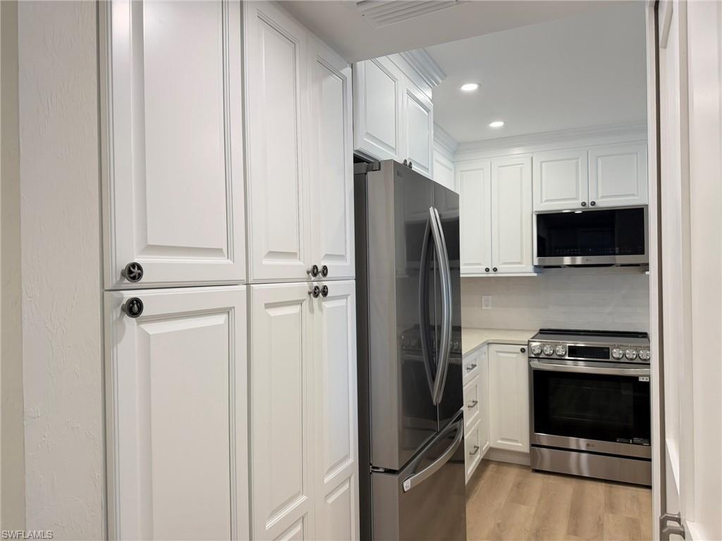 Kitchen with stainless steel appliances, white cabinetry, recessed lighting, light wood finished floors, and crown molding