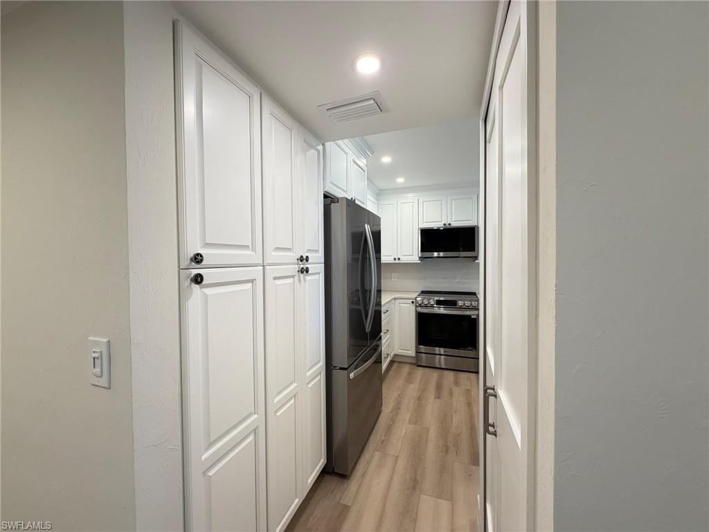 Kitchen featuring white cabinets, light wood-style flooring, appliances with stainless steel finishes, recessed lighting, and light countertops