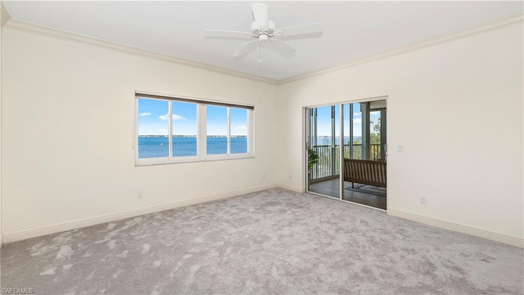 Empty room featuring carpet flooring, ornamental molding, ceiling fan, and a water view