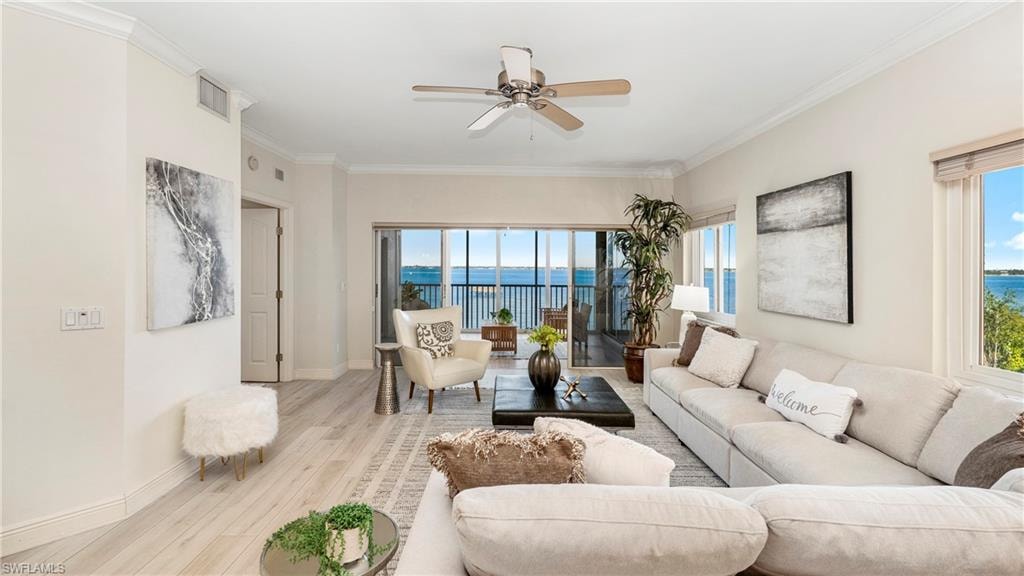 Living room featuring wood finished floors, ornamental molding, a water view, ceiling fan, and plenty of natural light