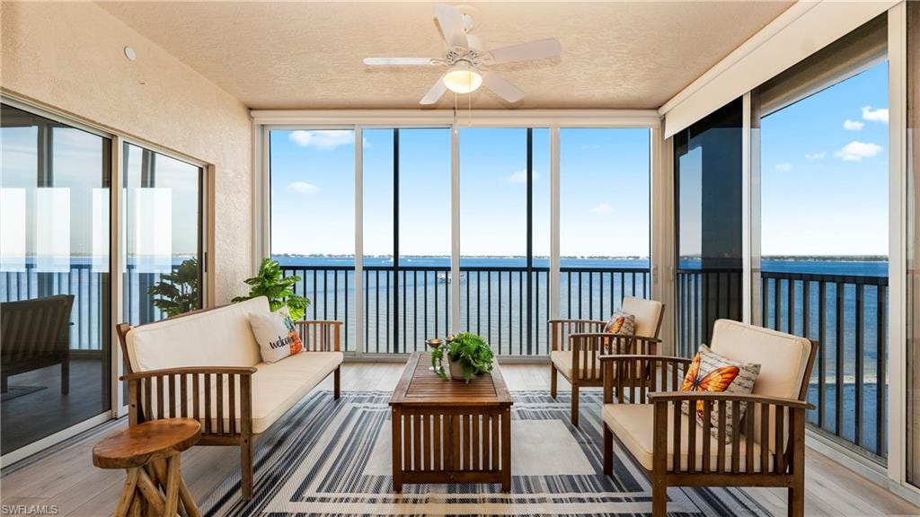 Sunroom featuring a water view, hardwood / wood-style floors, a textured ceiling, and expansive windows