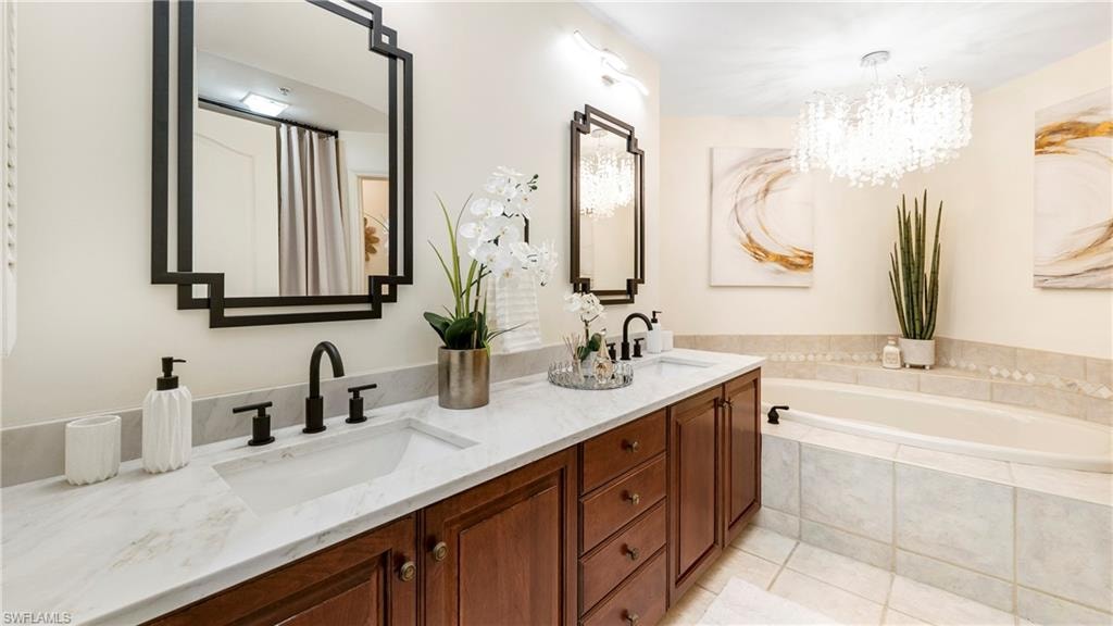 Bathroom featuring double vanity, a shower with curtain, light tile patterned floors, a bath, and a chandelier