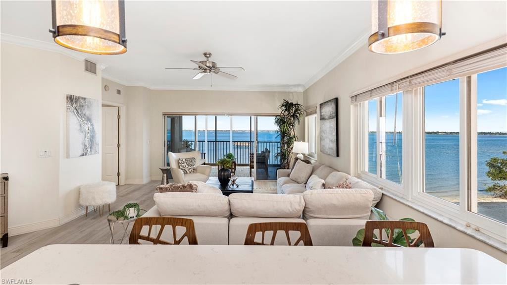 Living area featuring a water view, wood finished floors, crown molding, and a ceiling fan