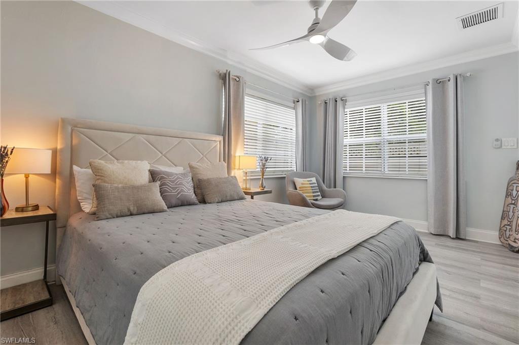 Bedroom with wood finished floors, ornamental molding, multiple windows, and ceiling fan