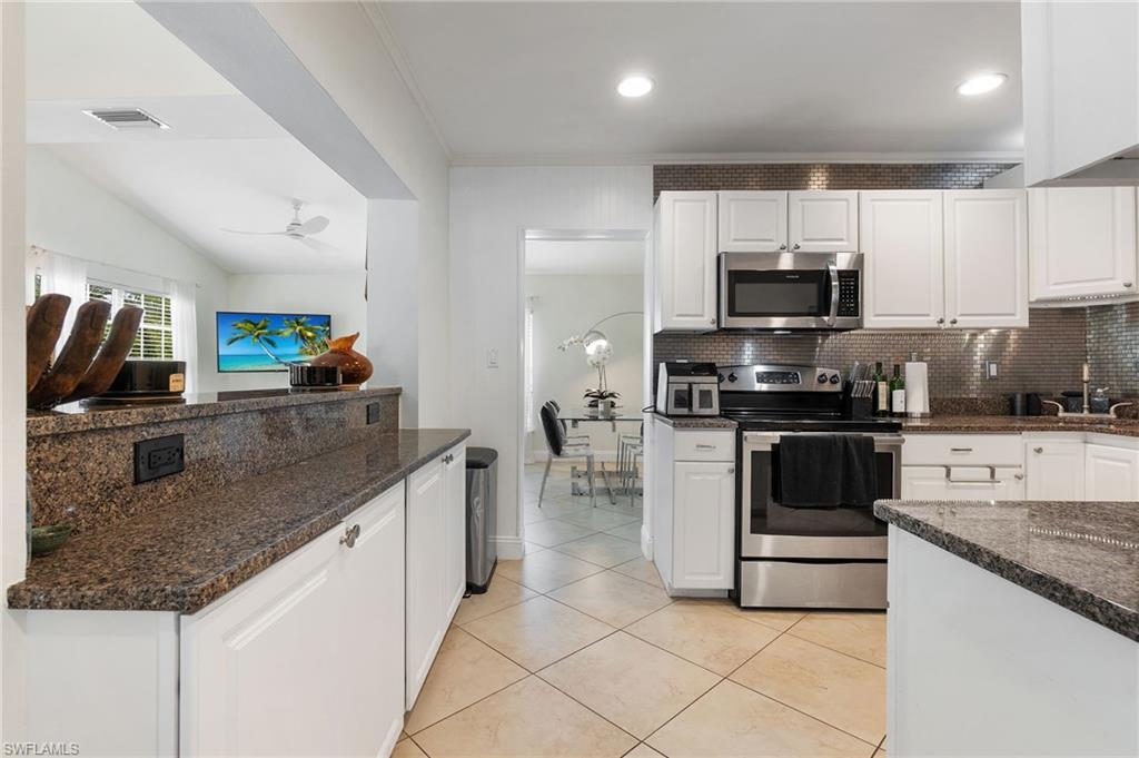 Kitchen with white cabinetry, appliances with stainless steel finishes, dark stone counters, tasteful backsplash, and crown molding