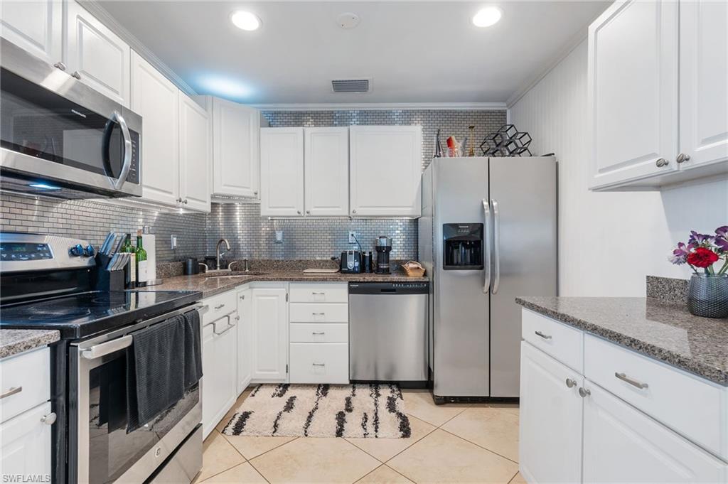 Kitchen with stainless steel appliances, white cabinetry, dark stone countertops, light tile patterned floors, and backsplash